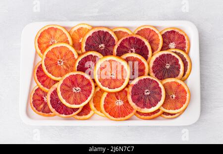 Sliced blood oranges circles on white plate on light background, top view, horizontal Stock Photo