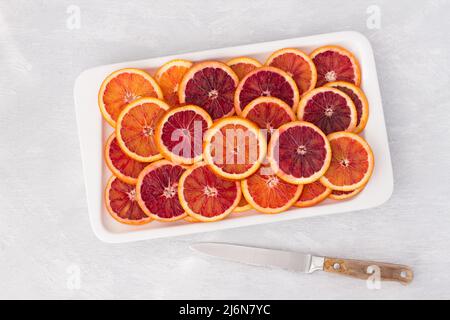 Sliced blood oranges circles on white plate on light background, top view, horizontal Stock Photo