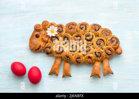 Easter lamb with poppy seeds, red colored eggs on a blue background. freshly baked homemade festive cake. top view Stock Photo