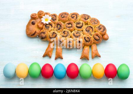 Easter lamb cake with poppy seeds, colorful eggs on a blue background. freshly baked homemade festive cake. top view Stock Photo