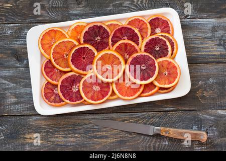 Sliced blood oranges circles on white plate on wooden table, top view, horizontal Stock Photo