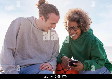 couple of young friends laughing while looking at mobile phone, concept of lifestyle and technology of communication Stock Photo