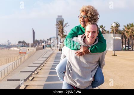 happy young couple smiling and having fun with the woman piggybacked by her boyfriend, concept of friendship and fun in a relationship, copy space for Stock Photo