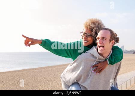 smiling young latin woman piggyback with her boyfriend having fun, concept of friendship and couple relationship, copy space for text Stock Photo