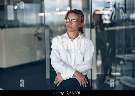 Focused business woman wearing eyeaglasses looks away during the working day at modern office Stock Photo