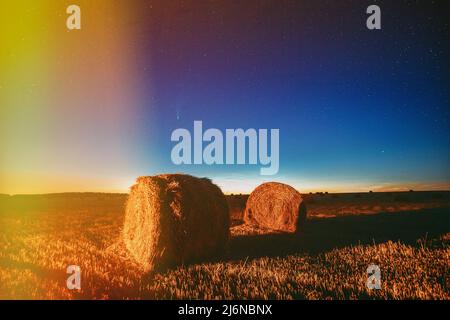 Comet Neowise In Night Starry Sky Above Haystacks In Summer Agricultural Field. Night Stars Above Rural Landscape With Hay Bales After Harvest Stock Photo