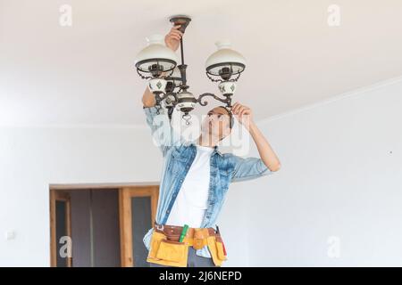 Handsome young builder is twisting the light bulb in. The man is looking up. Stock Photo