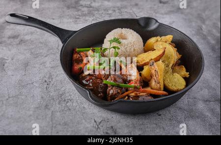 Peruvian d food - Lomo saltado - beef tenderloin with purple onion, yellow pepper, tomatoes served in a black pan with french fries and rice. Top view Stock Photo