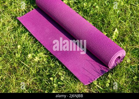 Rolled Yoga mat on green grass with sunlight, close up directly above. Outdoor sport concept Stock Photo