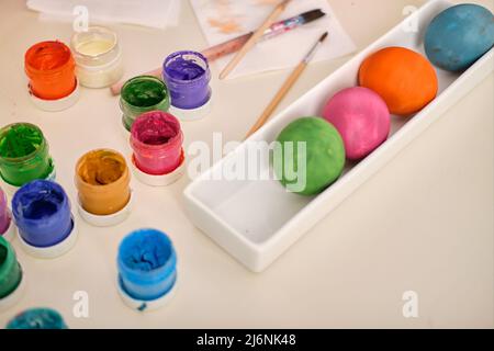 Painted multicolored wooden eggs, paints, brushes on a white table. Decorating eggs for Easter. Handmade Stock Photo