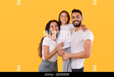 Arabic Parents And Daughter Embracing Together Posing On Yellow Background Stock Photo