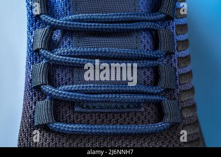 Laced up black blue mesh fabric sneakers macro. Laced fastening of new sport shoe on a blue background. Elastic laces of modern textile sneakers. Stock Photo