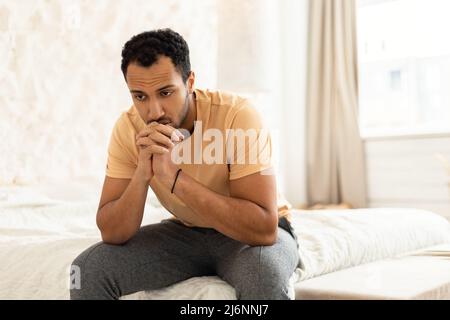 Depressed Middle Eastern Man Sitting Thinking In Modern Bedroom Stock Photo