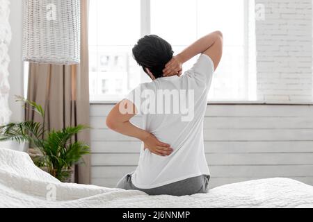 Unrecognizable man suffering from back pain at home in bedroom Stock Photo