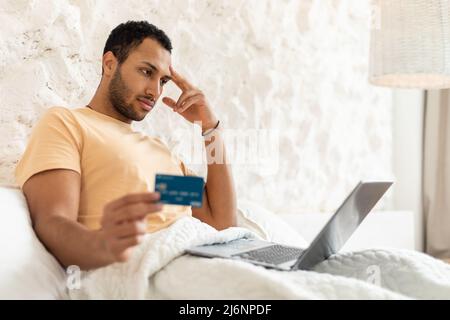 Middle Eastern Man Using Laptop And Credit Card In Bedroom Stock Photo