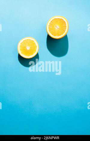 Simple concept flatlay two pieces of orange under the bright light with black shadows on blue background. Stock Photo