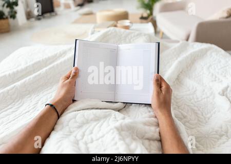 Man Holding Business Planner Planning Day Lying In Bedroom, POV Stock Photo