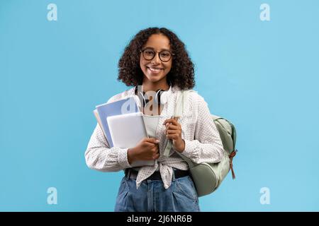 Online education. Smiling black female student with backpack and headphones holding notebooks and digital tablet Stock Photo