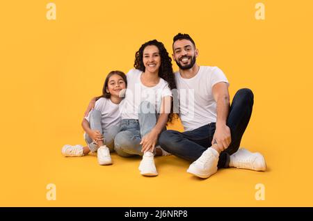 Middle Eastern Parents And Daughter Embracing Sitting On Yellow Background Stock Photo