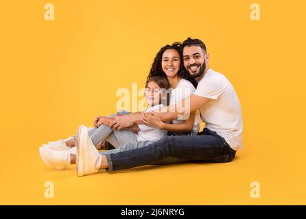 Arabic Family Of Three Embracing Together Sitting Over Yellow Background Stock Photo