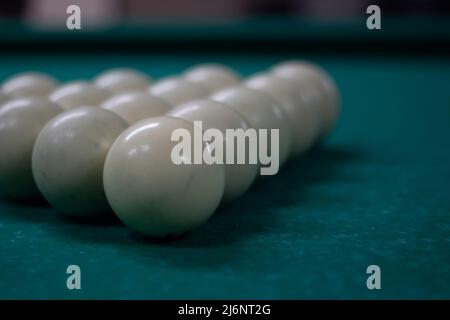 Billiard balls are collected in triangle. White balls on pool table. Details of sports equipment. Green cloth on table. Preparation of game. Stock Photo