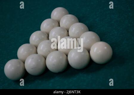 Billiard balls are collected in triangle. White balls on pool table. Details of sports equipment. Green cloth on table. Preparation of game. Stock Photo