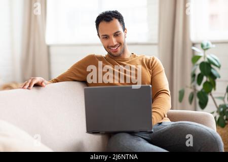Arab man using laptop sitting on couch at home Stock Photo