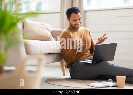 Arab guy making videocall using laptop sitting on floor Stock Photo