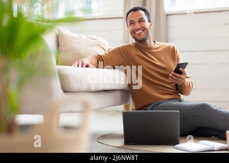 Young Arab man holding phone using pc at home Stock Photo