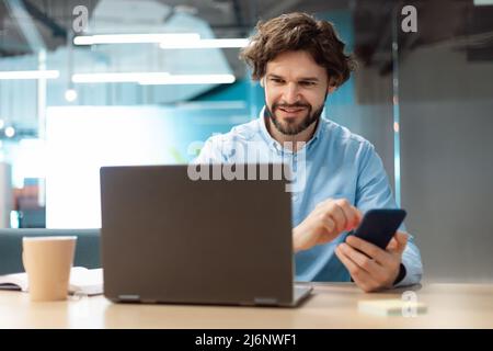 Portrait of smiling man using smartphone and pc at office Stock Photo