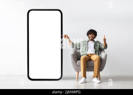 Handome young indian man pointing at huge smartphone, mockup Stock Photo
