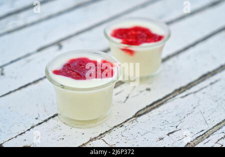 Healthy homemade plain yogurt in small glass cup, topping with organic strawberry jam, yogurt cup are on rustic white wooden table. Stock Photo