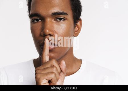 Young black man showing silence gesture and looking at camera isolated over white wall Stock Photo