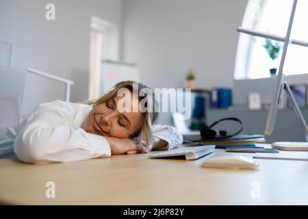 Middle aged business woman taking a nap right at the workplace. Overworked female office worker Stock Photo