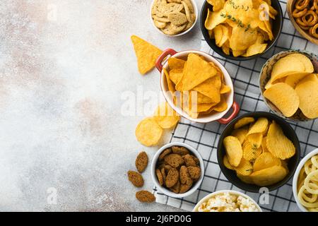 Snacks. Unhealthy food. All classic potato snacks with peanuts, popcorn and onion rings and salted pretzels in bowl plates on gray concrete background Stock Photo