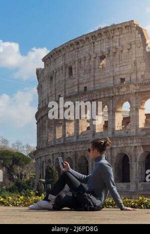 Young man with bun on his smartphone while sitting relaxed resting with the Rome coliseum in the background Stock Photo