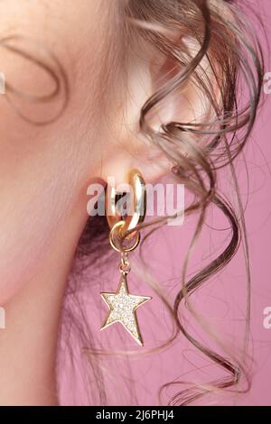 Women's neck and ear with an earring on a pink background. Female with curly strands of hair. Stock Photo