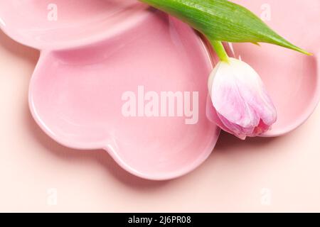Spring table setting - empty pink plate in form of heart and pink tulip close up on pastel pink background. Holiday mock up. Copy space for text or de Stock Photo