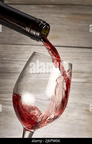 bottle pouring red wine in a glass isolated on rustic wooden background Stock Photo