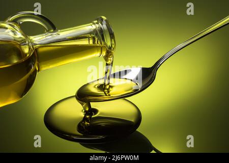 oil poured in a spoon overflowing on green background Stock Photo