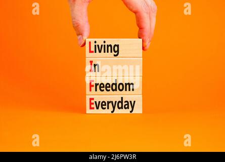 LIFE living in freedom everyday symbol. Concept words LIFE living in freedom everyday on blocks on orange background. Businessman hand. Business LIFE Stock Photo