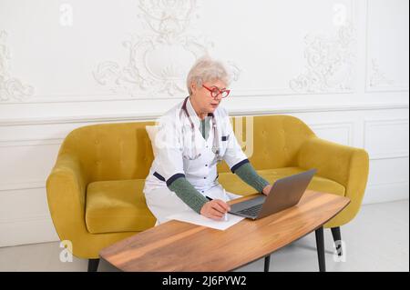 Middle age female doctor using laptop, writing notes with stethoscope on table. Healthcare concept. Medical doctor writing and taking notes Stock Photo