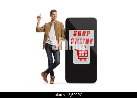 Full length portrait of a casual man pointing and leaning on a smartphone with sign for online shopping isolated on white background Stock Photo