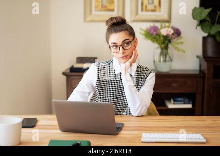 Beautiful young woman looking thoughtfully while sitting at desk at home and working. Home office. Stock Photo