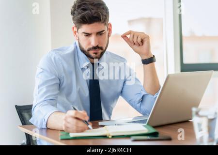 Thinking businessman using laptop and making notes while working at the office. Stock Photo