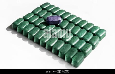green Pills of chlorella, spirulina, barley grass close-up lined up in rows and one purple tablet on top on white background Nutritional supplement, d Stock Photo