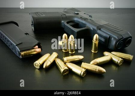 9 mm handgun with fully loaded magazine and bunch of golden brass ammo spilled on black wooden desk Stock Photo