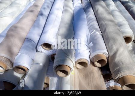 White fabric rolls stack on textile stall outdoor market. Stock Photo