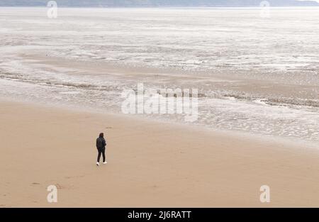 Lone figure on Weston-super-Mare beach, smartphone in hand, walking out to a sea of mud Stock Photo