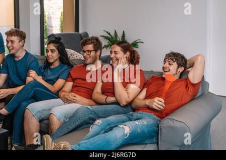 friends enjoying together their favourite sport broadcast on television competing for their team. youngsters partying Stock Photo